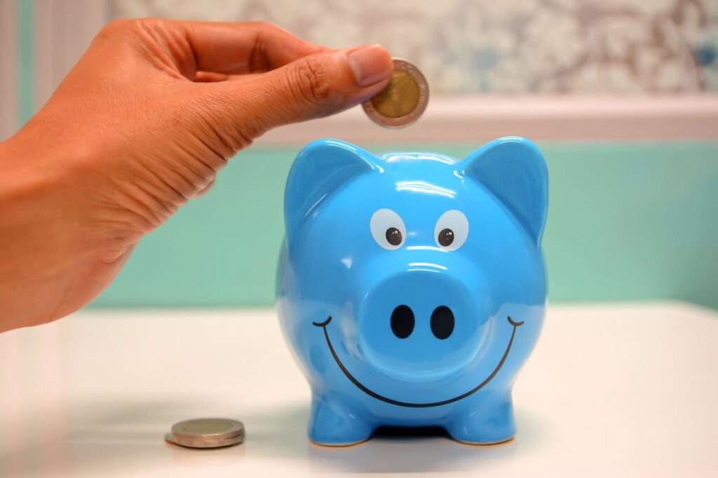 pexels photo 1602726 Hand inserting a coin into a blue piggy bank for savings and money management.