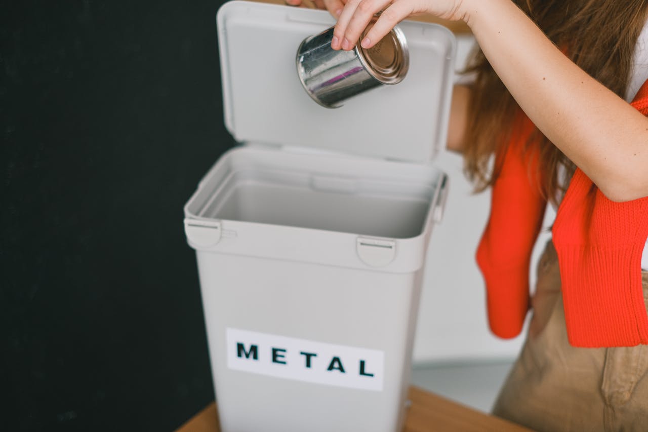 services-01 A woman recycling a metal tin can into a labeled bin indoors. Promotes sustainability.